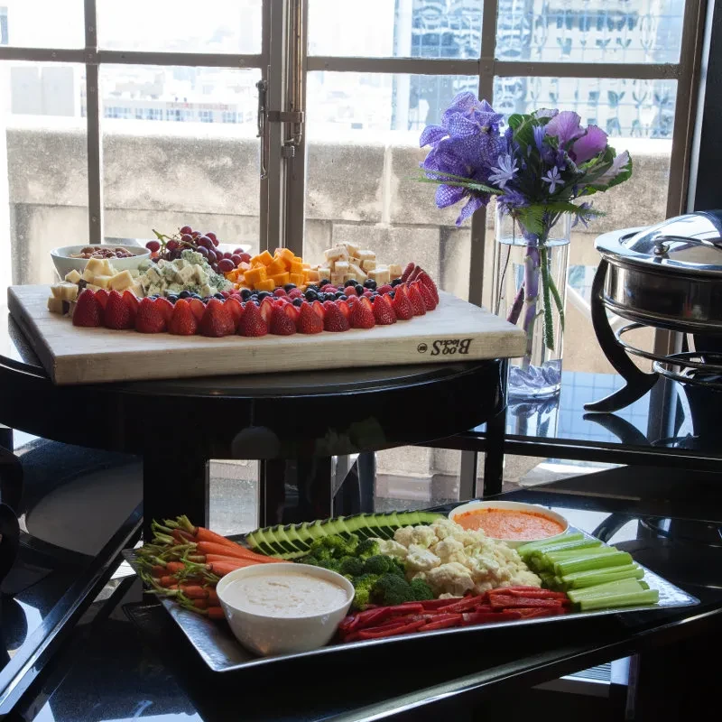Elegant buffet with fruit, cheese, crudités platters, and city skyline view.