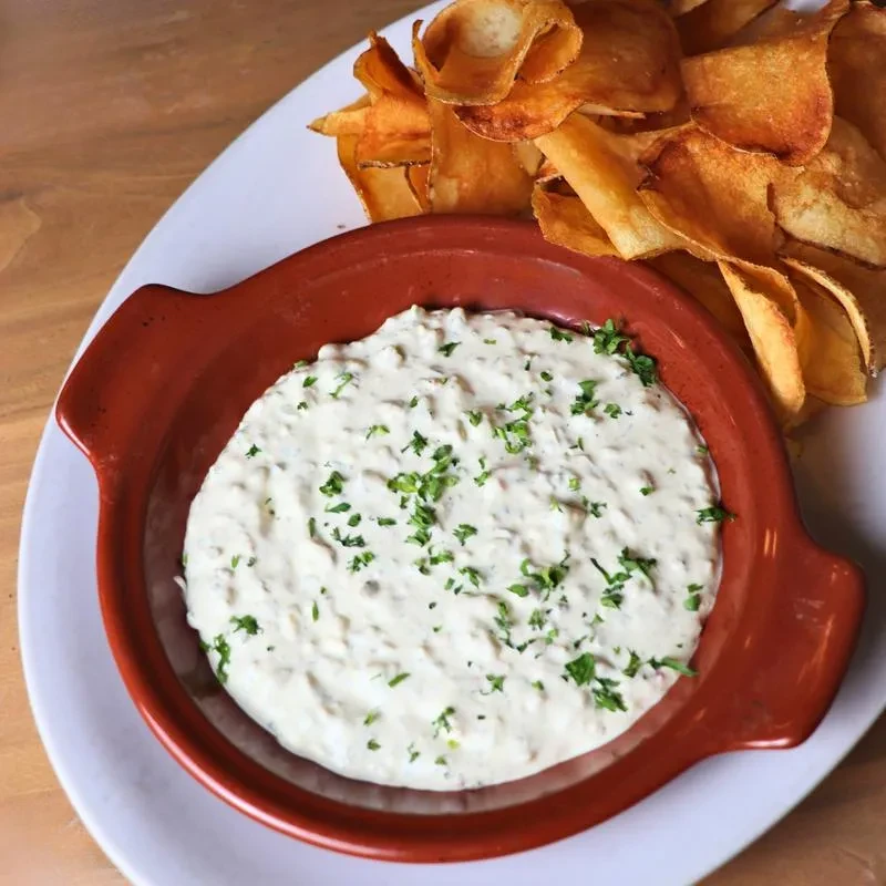 Rustic bowl of creamy dip with herbs and golden potato chips.