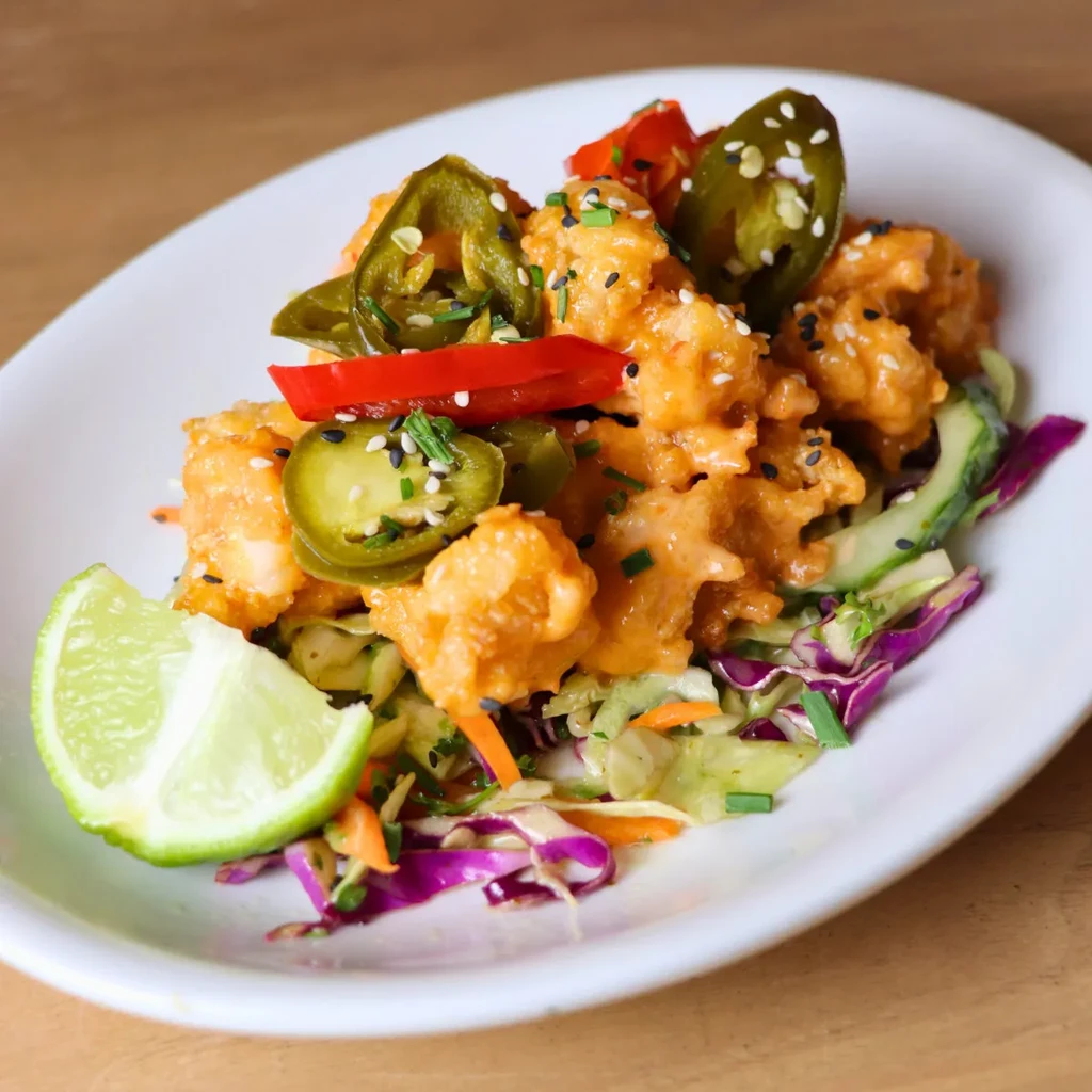 Fried shrimp in orange sauce on colorful coleslaw with lime.