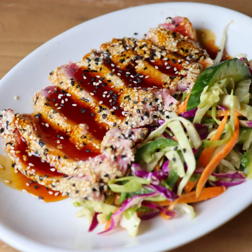 Plated seared sesame tuna, rare center, with sauce and cabbage-carrot slaw.