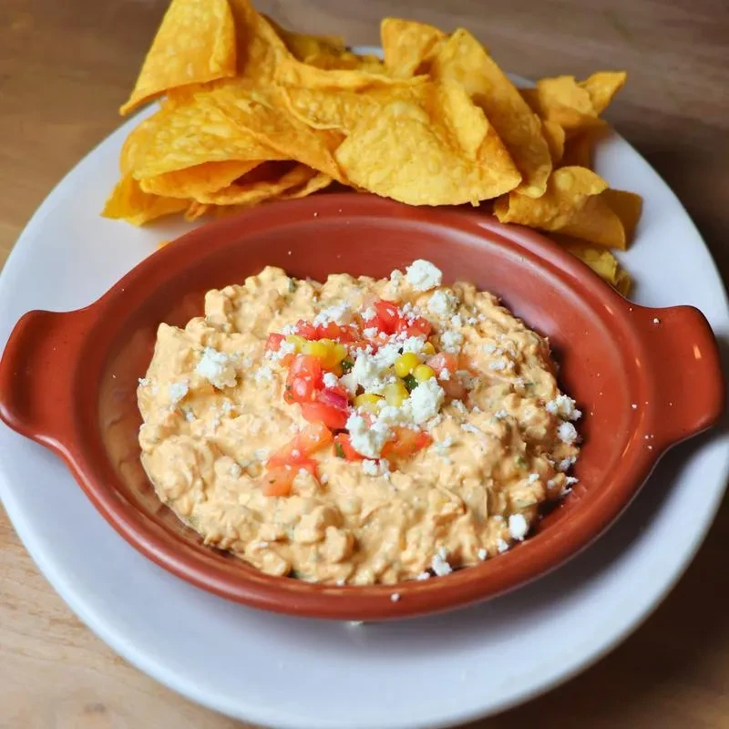 Creamy orange dip with tomatoes, corn, cheese, and tortilla chips.