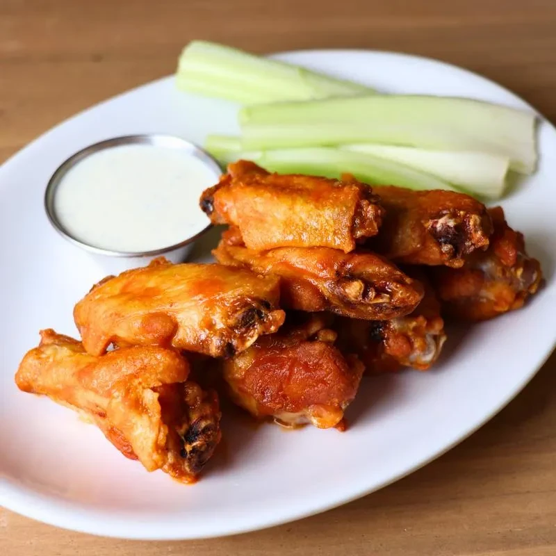 Oval plate of orange-red hot wings, white dip, and celery.