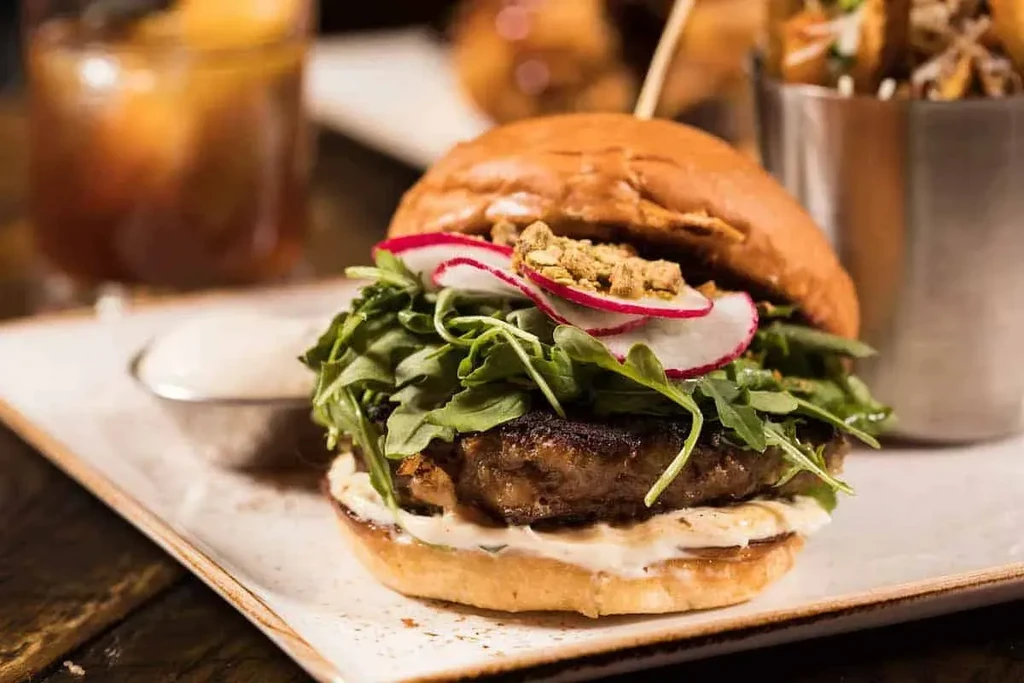 Gourmet burger with arugula, radish, golden topping, and creamy sauce.