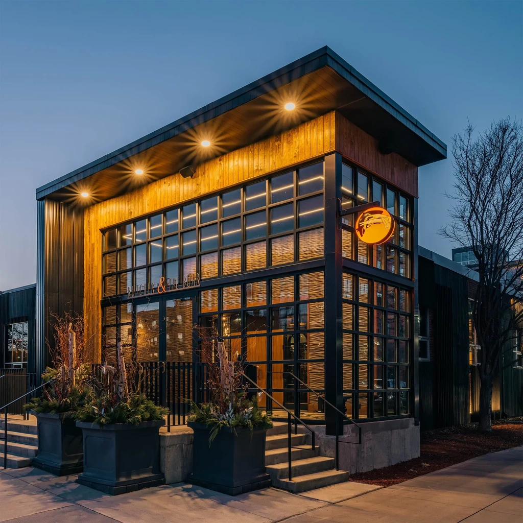 Modern restaurant exterior at dusk with cantilevered roof and fish logo.
