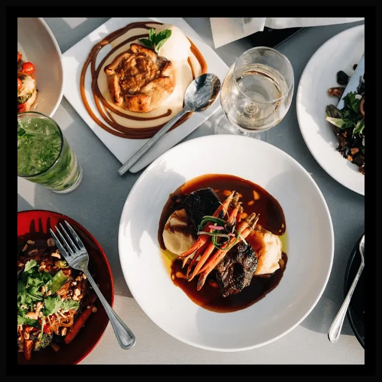 Table with braised meat, noodles, dessert, salad, and two types of drinks.