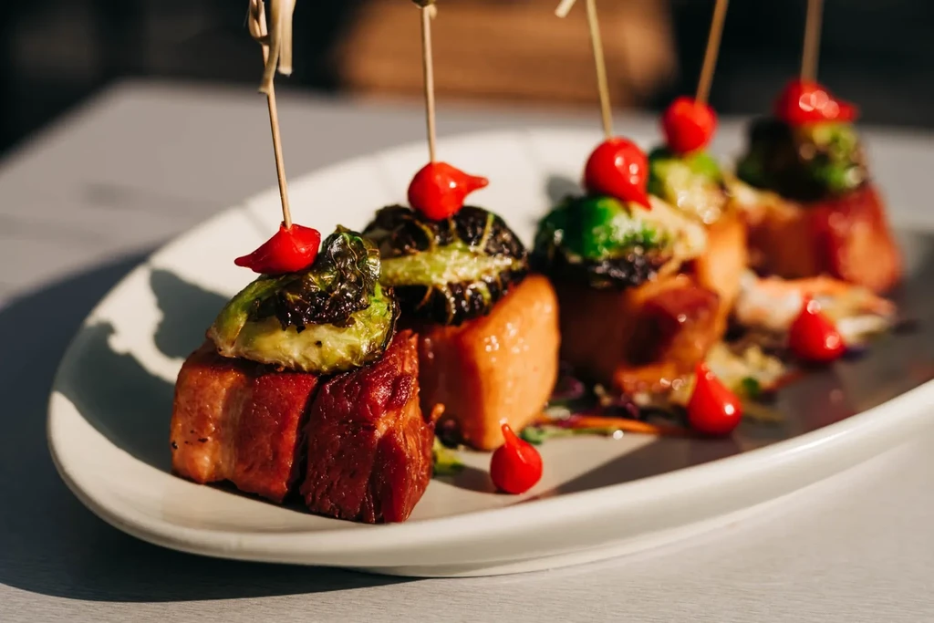 Skewered bacon-wrapped appetizers with sprouts and peppers on white plate.