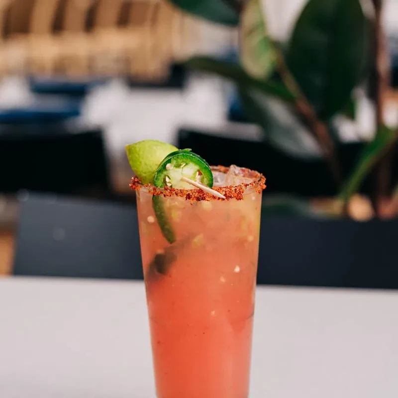 Reddish-pink cocktail with a chili-lime rim, lime, and jalapeño garnish.