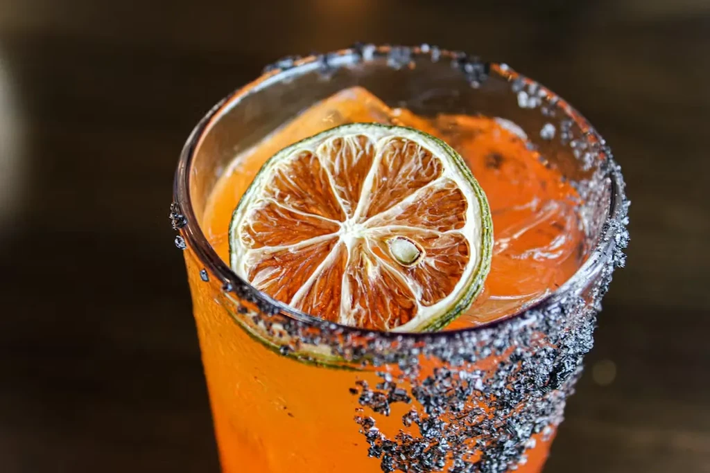 Vibrant orange cocktail with ice, dried citrus garnish, and dark rim.