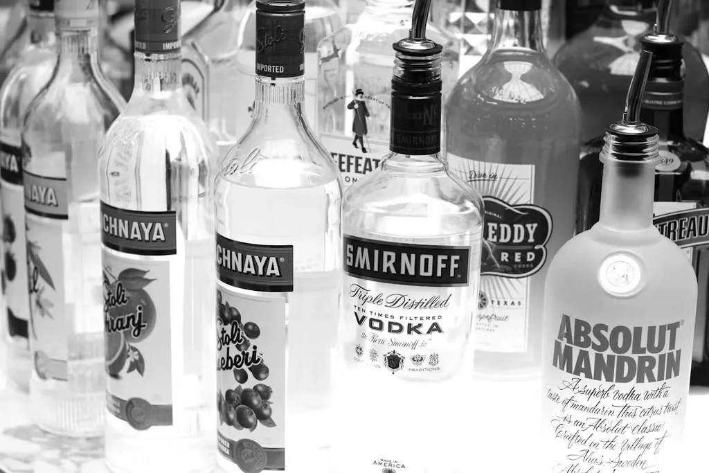 Black and white photo of many liquor bottles, some with pour spouts.