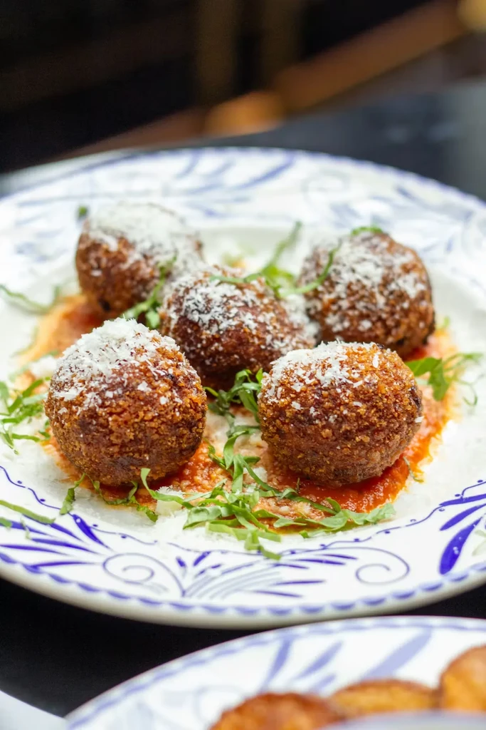 Five golden-brown arancini with Parmesan, marinara, and fresh herbs.
