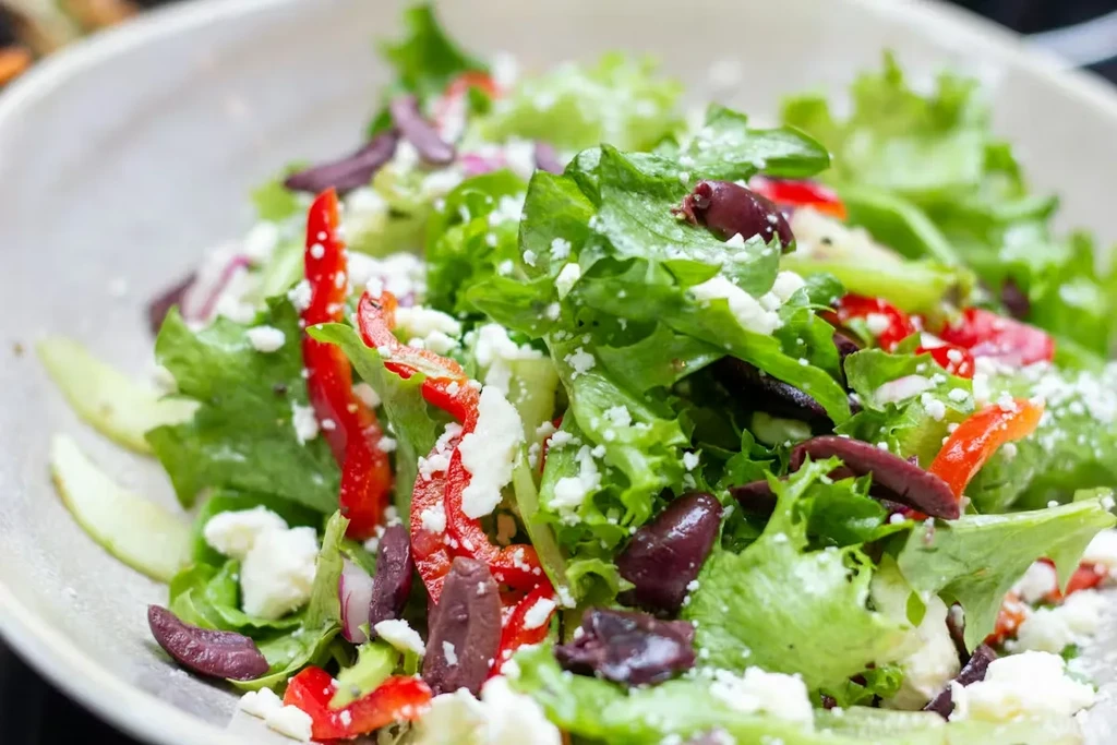 Close-up of a vibrant salad with lettuce, bell pepper, olives, and feta.
