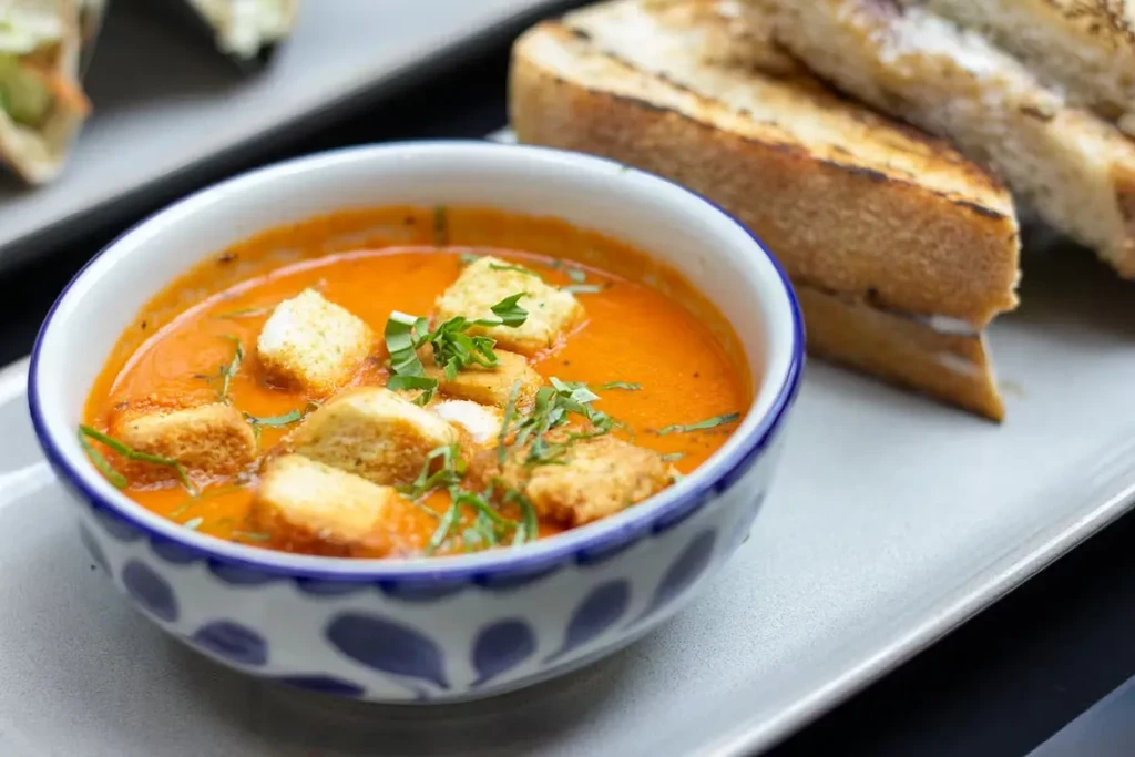 Creamy orange soup with croutons, herbs, and toasted bread.