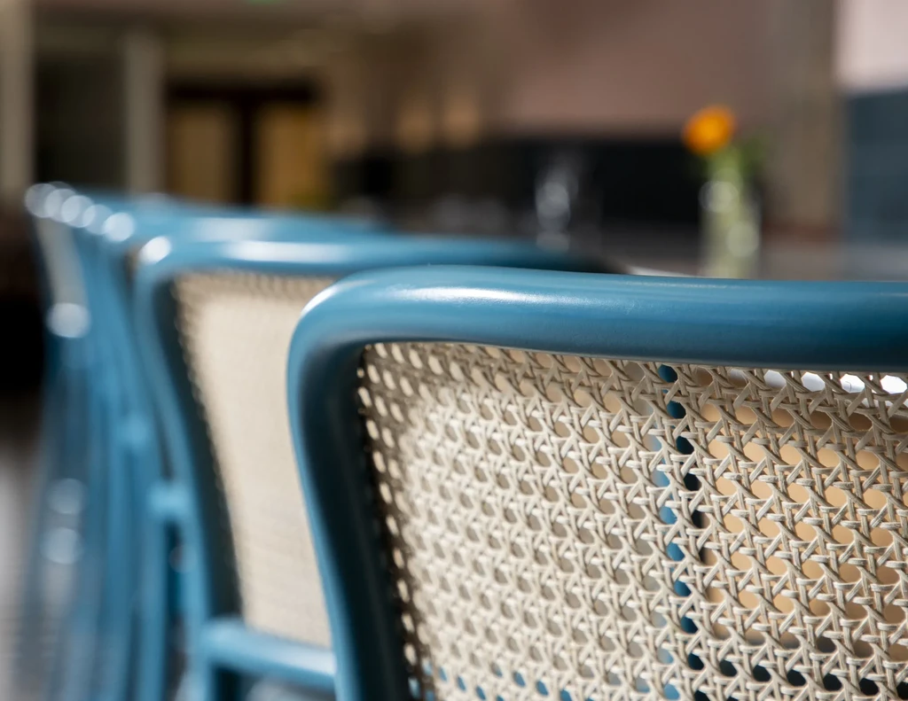 Row of modern bar stools with teal frames and cane backs.