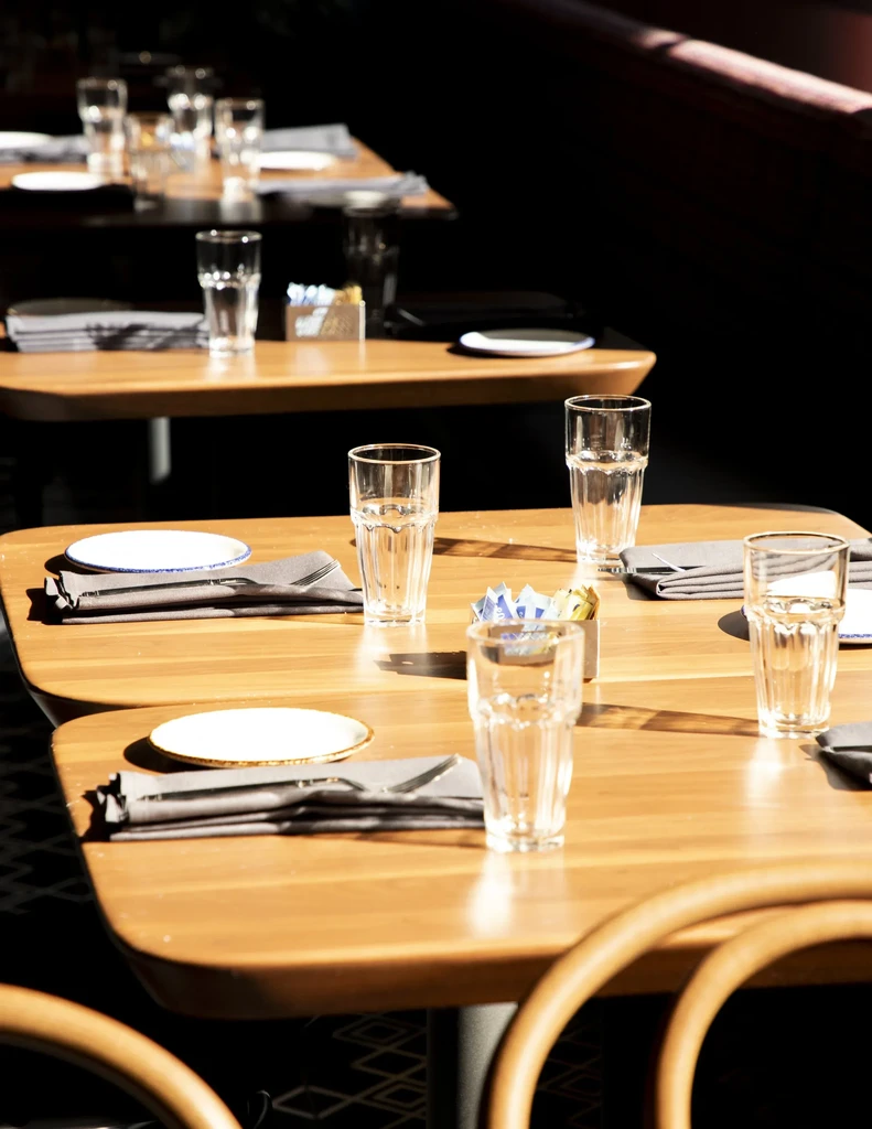Brightly lit, empty restaurant with meticulously set wooden dining tables.