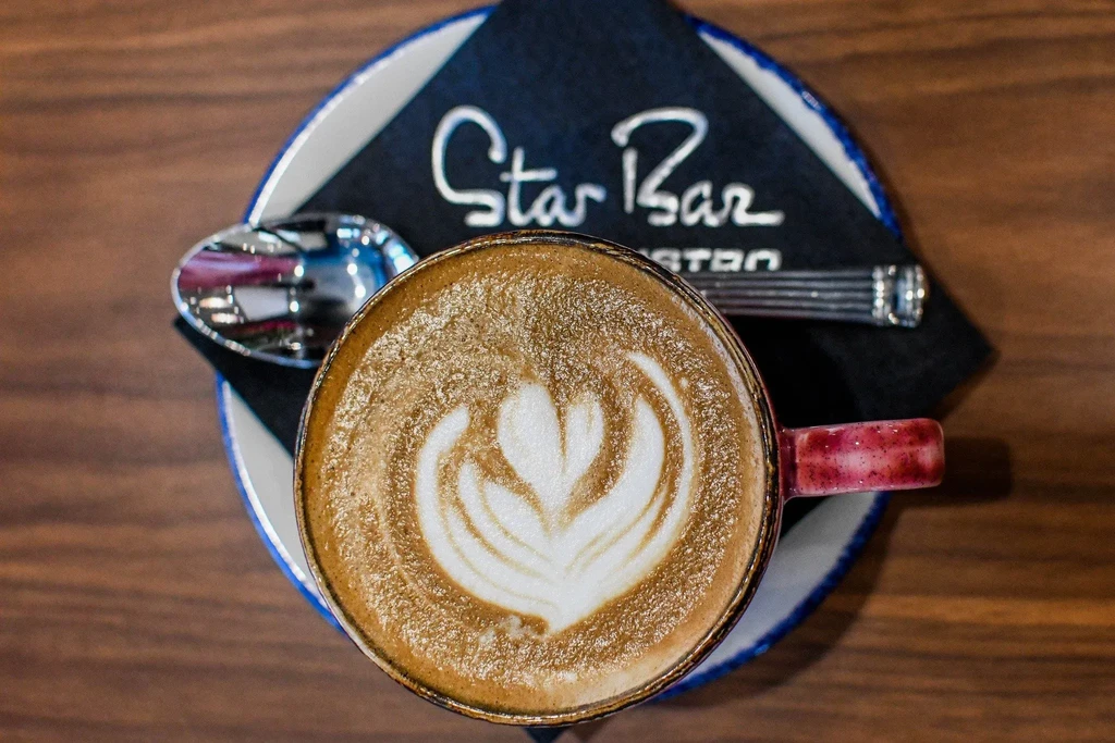 Intricate latte art cappuccino on "Star Bar" napkin, wooden table.