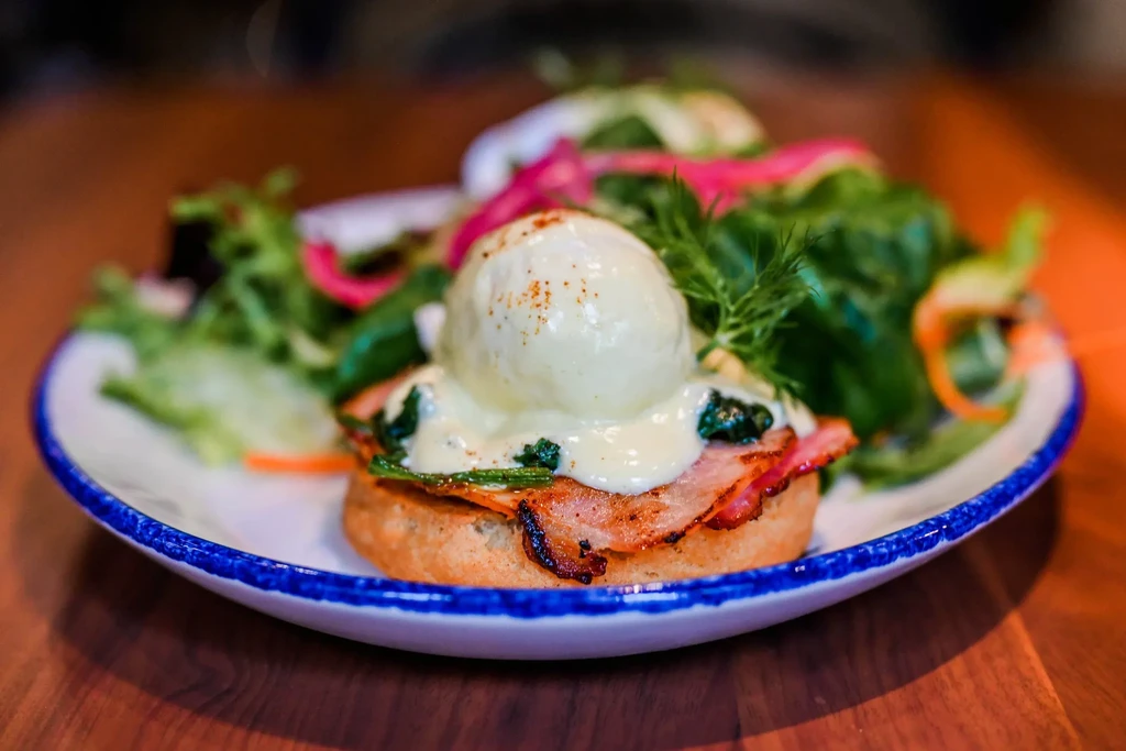 Eggs Benedict with crispy bacon, spinach, hollandaise, and fresh side salad.