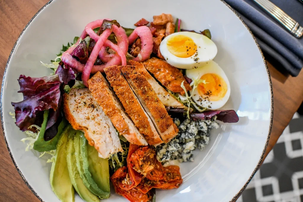 Colorful salad bowl with grilled chicken, avocado, eggs, and pickled onions.