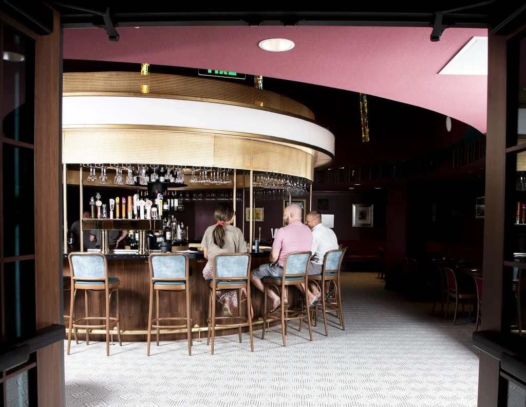 Circular bar with gold stripes, bottles, glasses, taps, and three patrons.