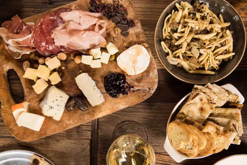 Overhead shot: Rustic charcuterie board, pasta, bread, wine on wooden table.