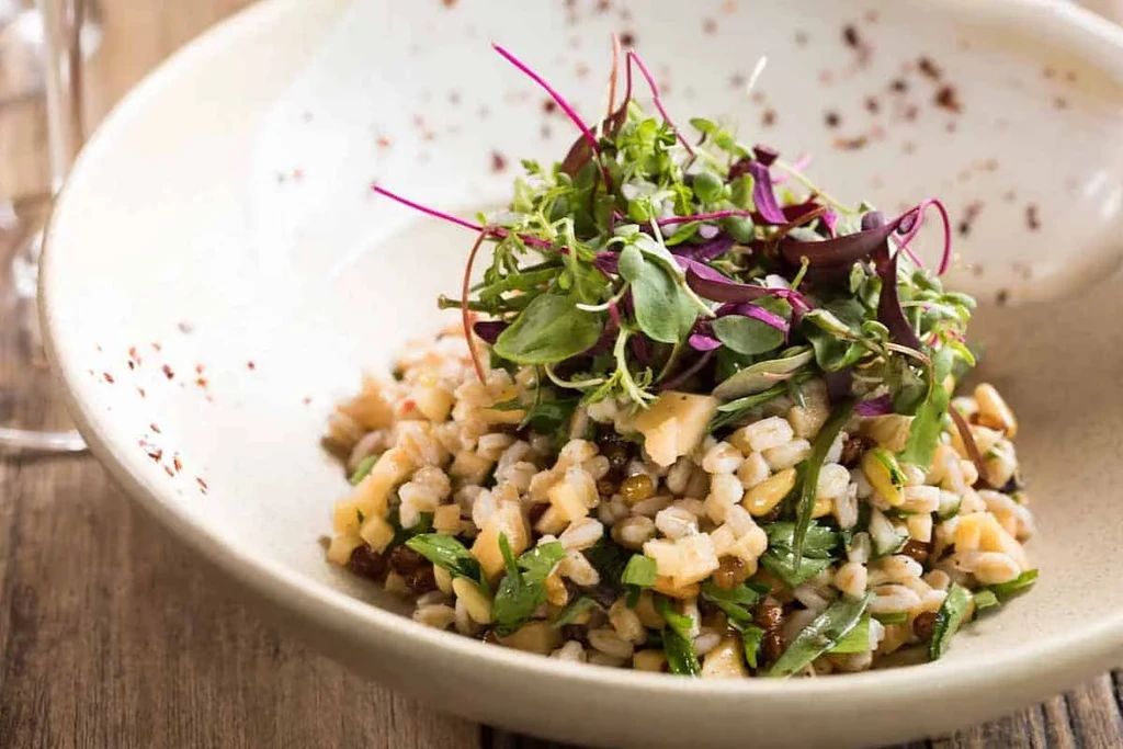 Grain salad with greens, dried fruit, and nuts in a speckled ceramic bowl.