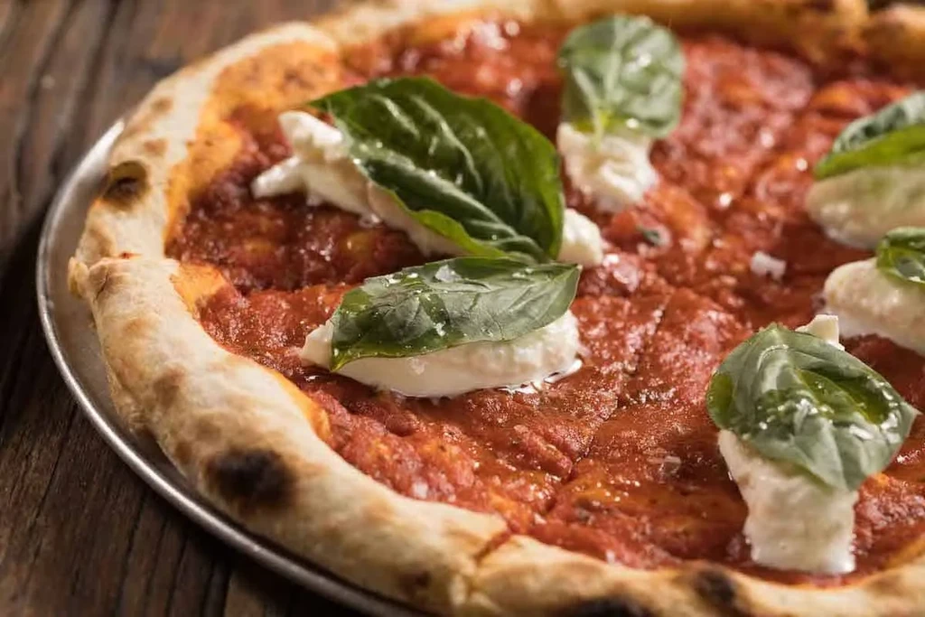 Freshly baked pizza with tomato, mozzarella, and basil on a pan.