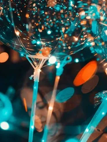 Close-up of transparent balloons glowing blue and orange, on illuminated sticks.
