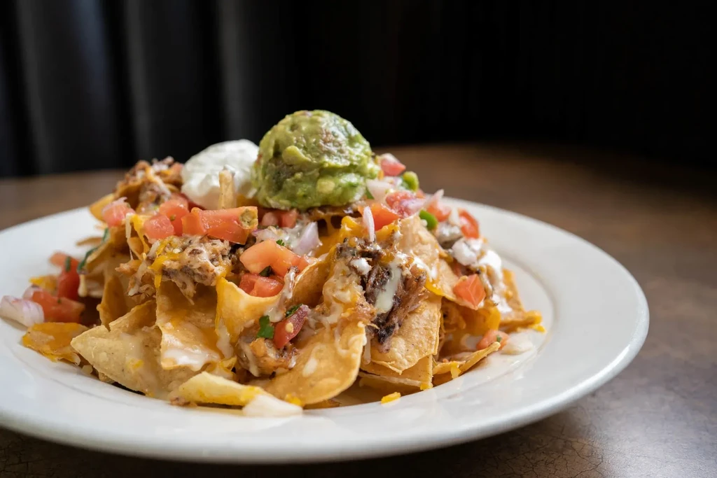 Close-up: Loaded nachos with cheese, meat, tomatoes, onions, guacamole, sour cream.