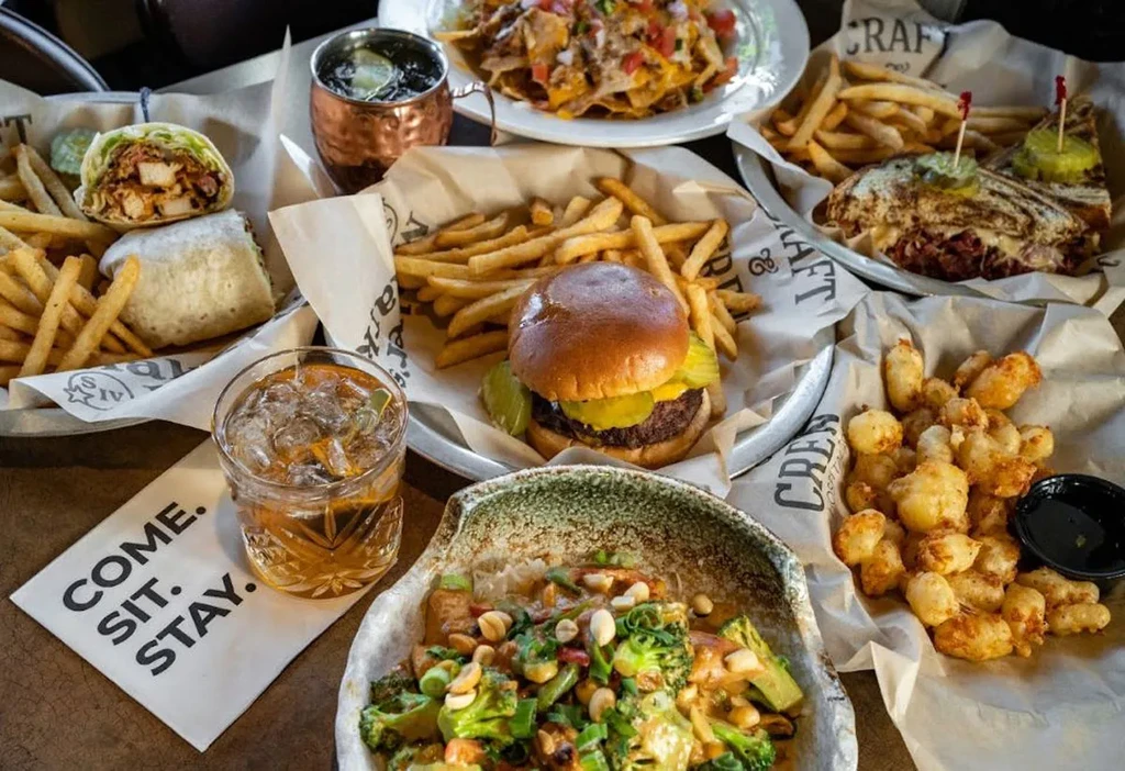 Overhead shot of a pub table with burgers, nachos, sandwiches, and drinks.