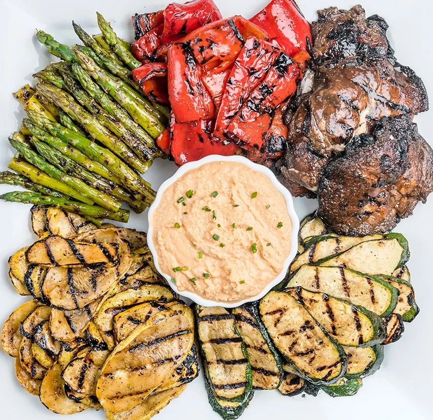 Overhead platter of assorted grilled vegetables with a creamy dip.