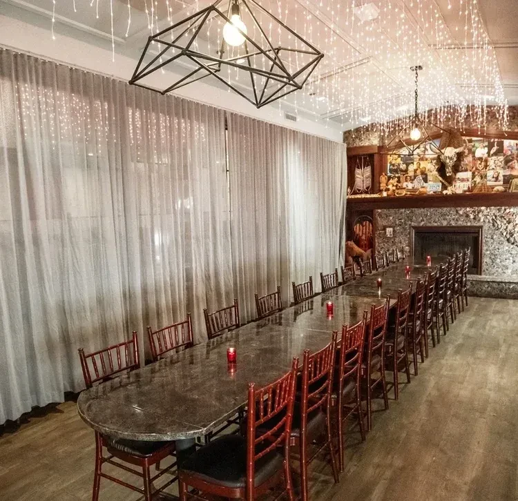 Oval dining table, red chairs, stone fireplace, chandeliers, and string lights.
