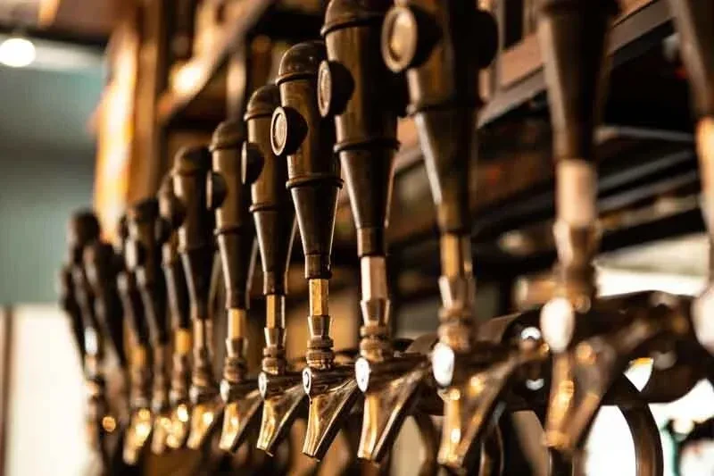 Antique-style dark beer taps gleaming in a softly lit bar.