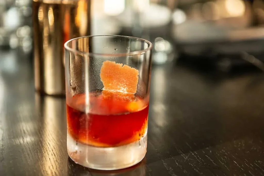 A dark reddish-orange cocktail in a short glass with orange peel.