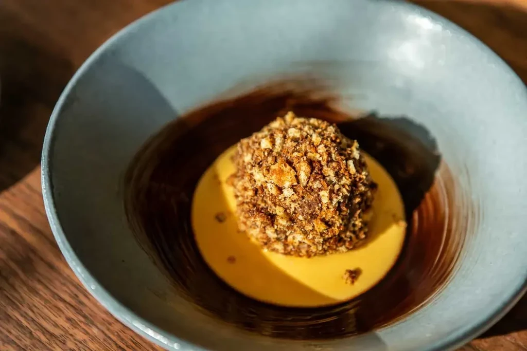Crumble-topped dome dessert, yellow and chocolate sauces in a bowl.