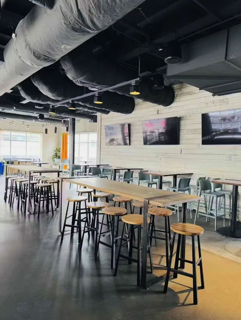 Empty modern restaurant with exposed ductwork, high-top tables, and large windows.