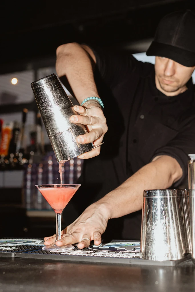 Bartender pours pink cocktail from shaker into martini glass.