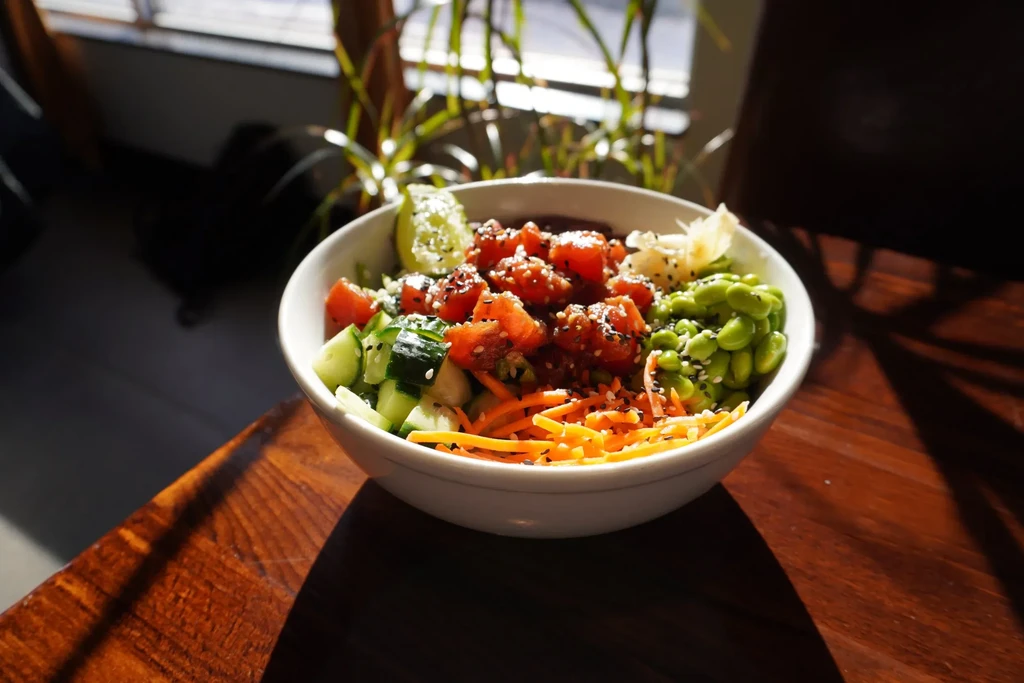 Vibrant poke bowl with red protein, edamame, cucumbers, carrots, and lime.
