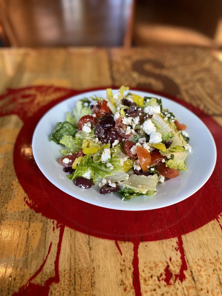 Greek salad with feta, olives, and peppers on a wooden table.