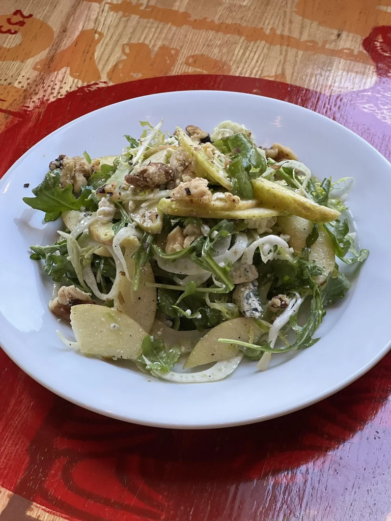 Salad with dark greens, pear, blue cheese, walnuts on patterned table.