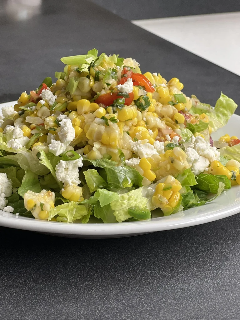Vibrant corn salad with cheese and tomatoes on a white plate.