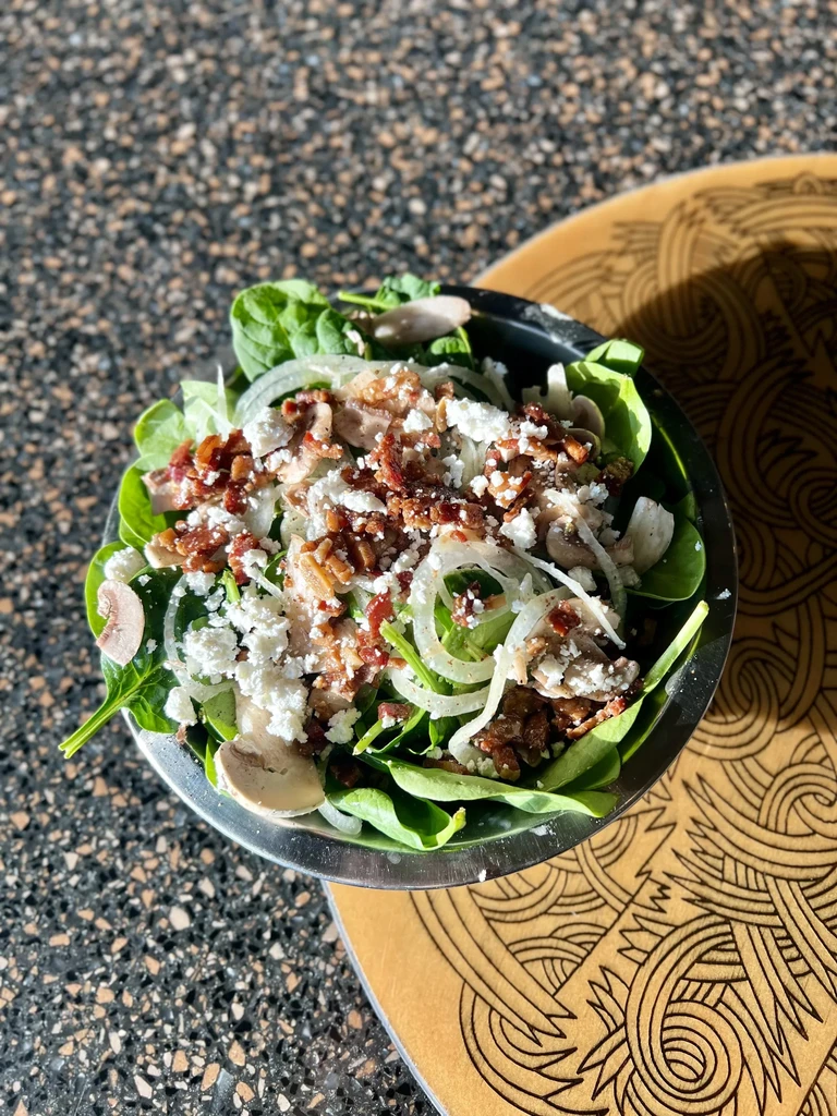 Top-down spinach salad with bacon, cheese, mushrooms in metallic bowl.