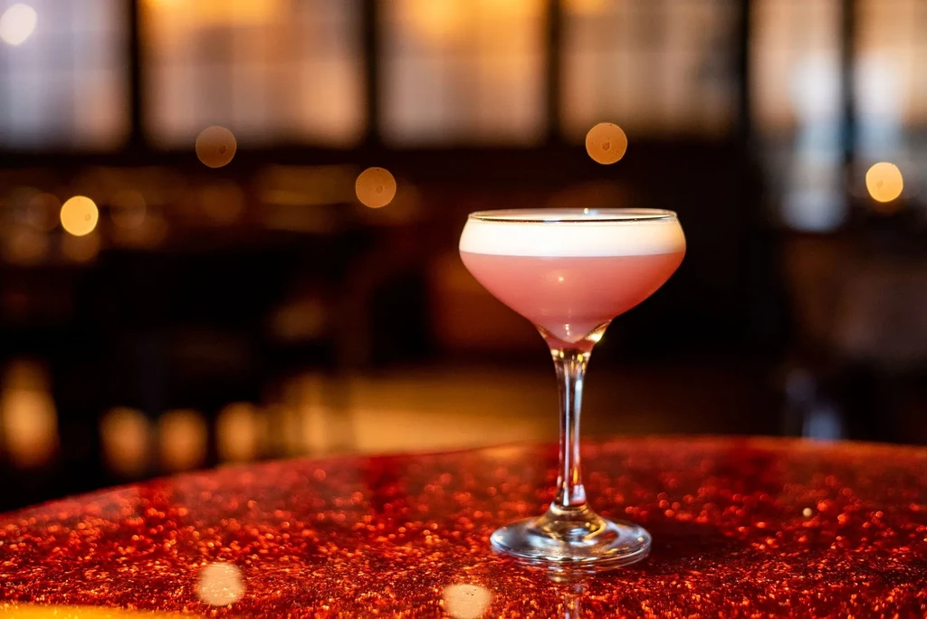 Pink cocktail with white foam in coupe glass on red table.