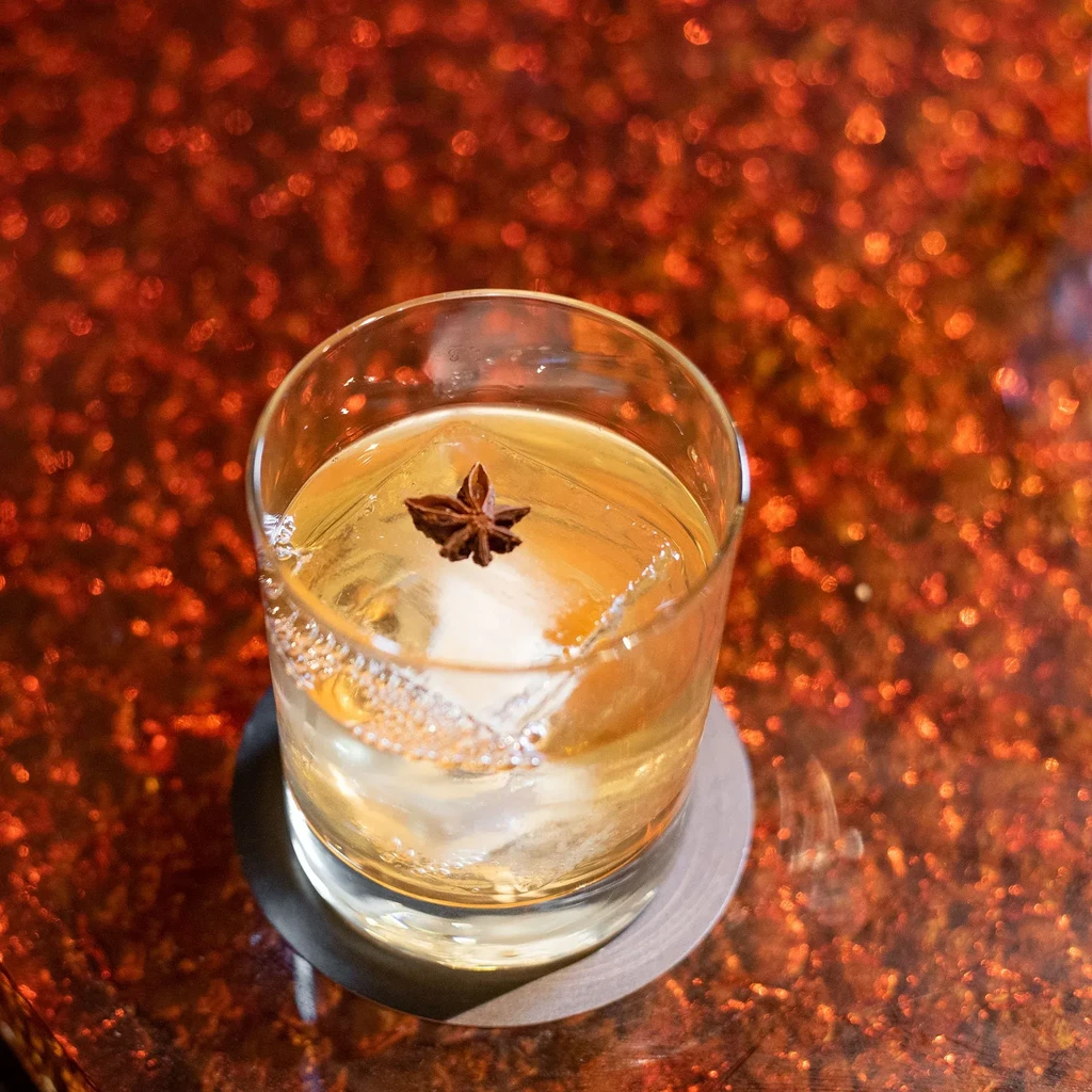 Rocks glass with amber cocktail, large ice cube, and star anise.