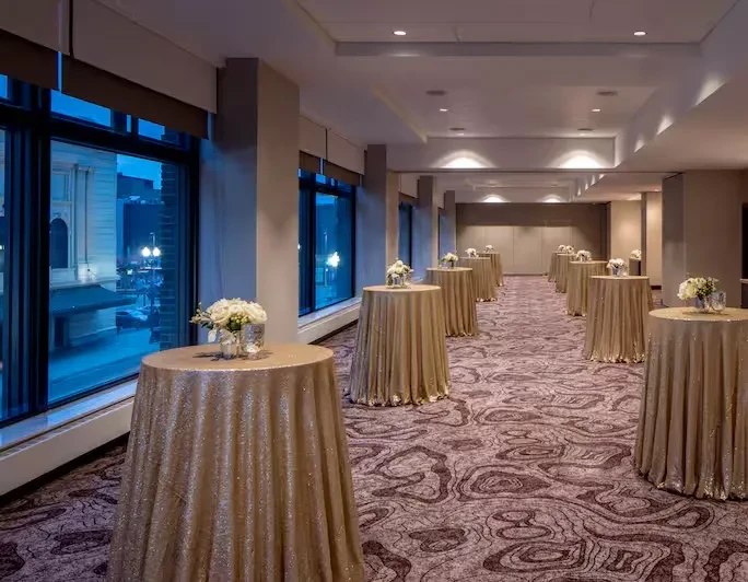 Elegant ballroom with gold sequined cocktail tables and city view at dusk.