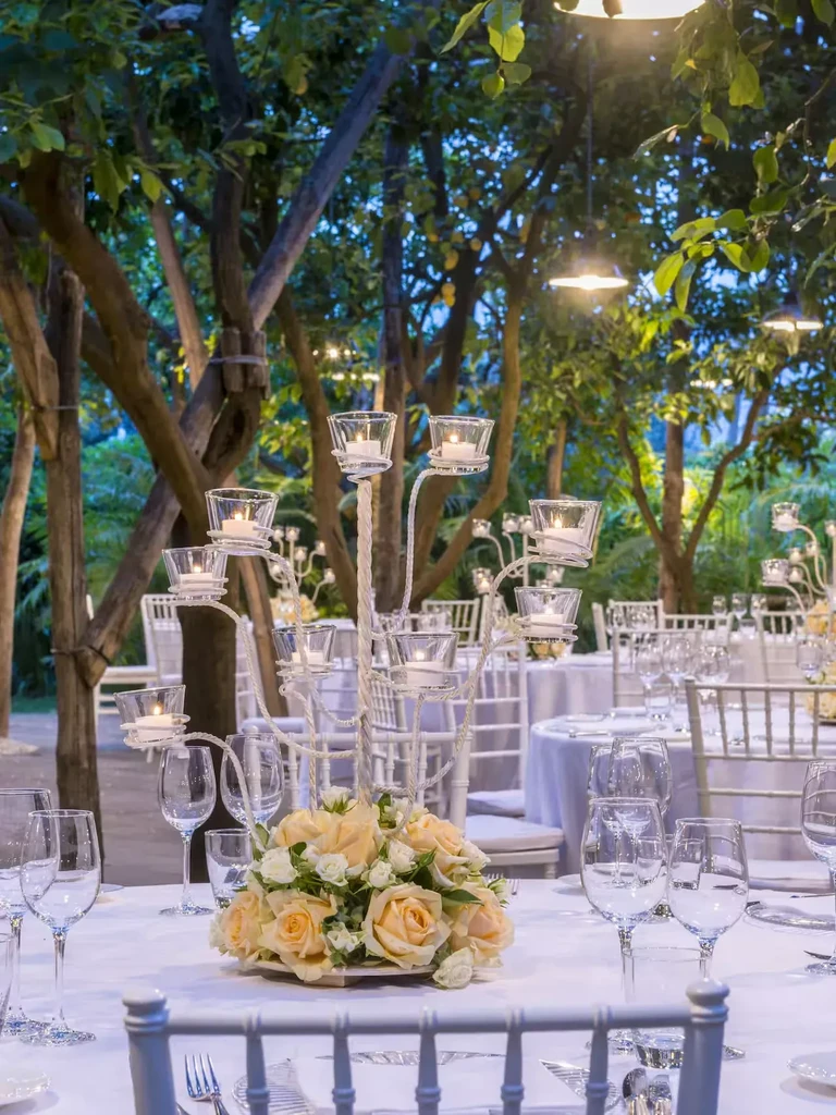 Outdoor dining table with peach roses, white flowers, and glowing candles.