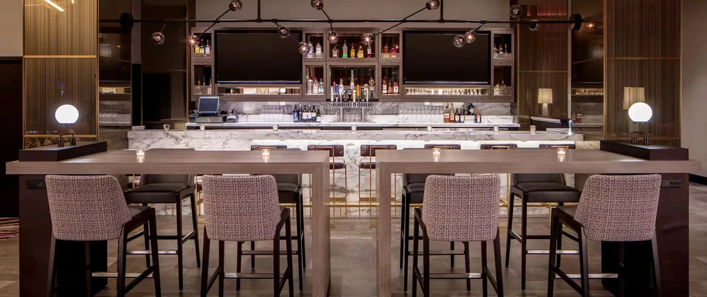 Upscale bar with white marble counter, extensive liquor display, and high-top tables.
