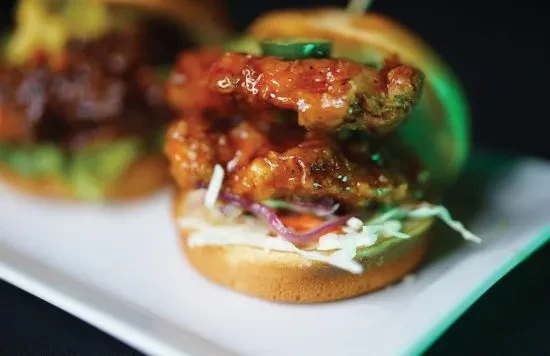 Two glazed fried chicken sliders with slaw on a white plate.