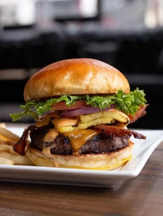 Close-up of a hamburger with cheese, bacon, pineapple, and fries.