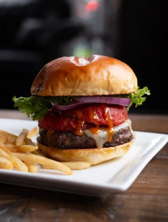 Gourmet burger with melted cheese, red sauce, and golden fries.
