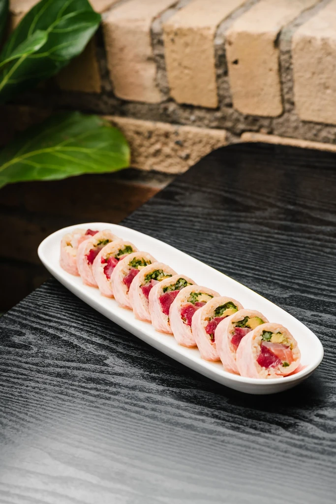 Pink-wrapped sushi rolls with tuna, avocado, and greens on a white dish.