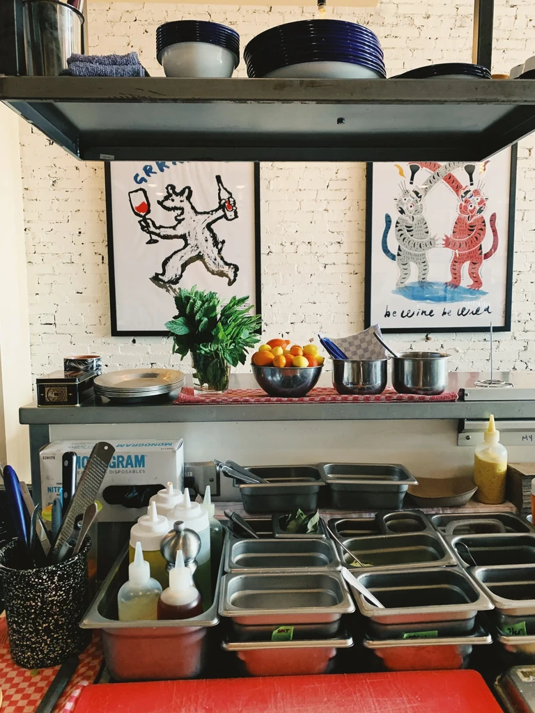 Restaurant prep counter with stainless steel, kitchen tools, and whimsical art.
